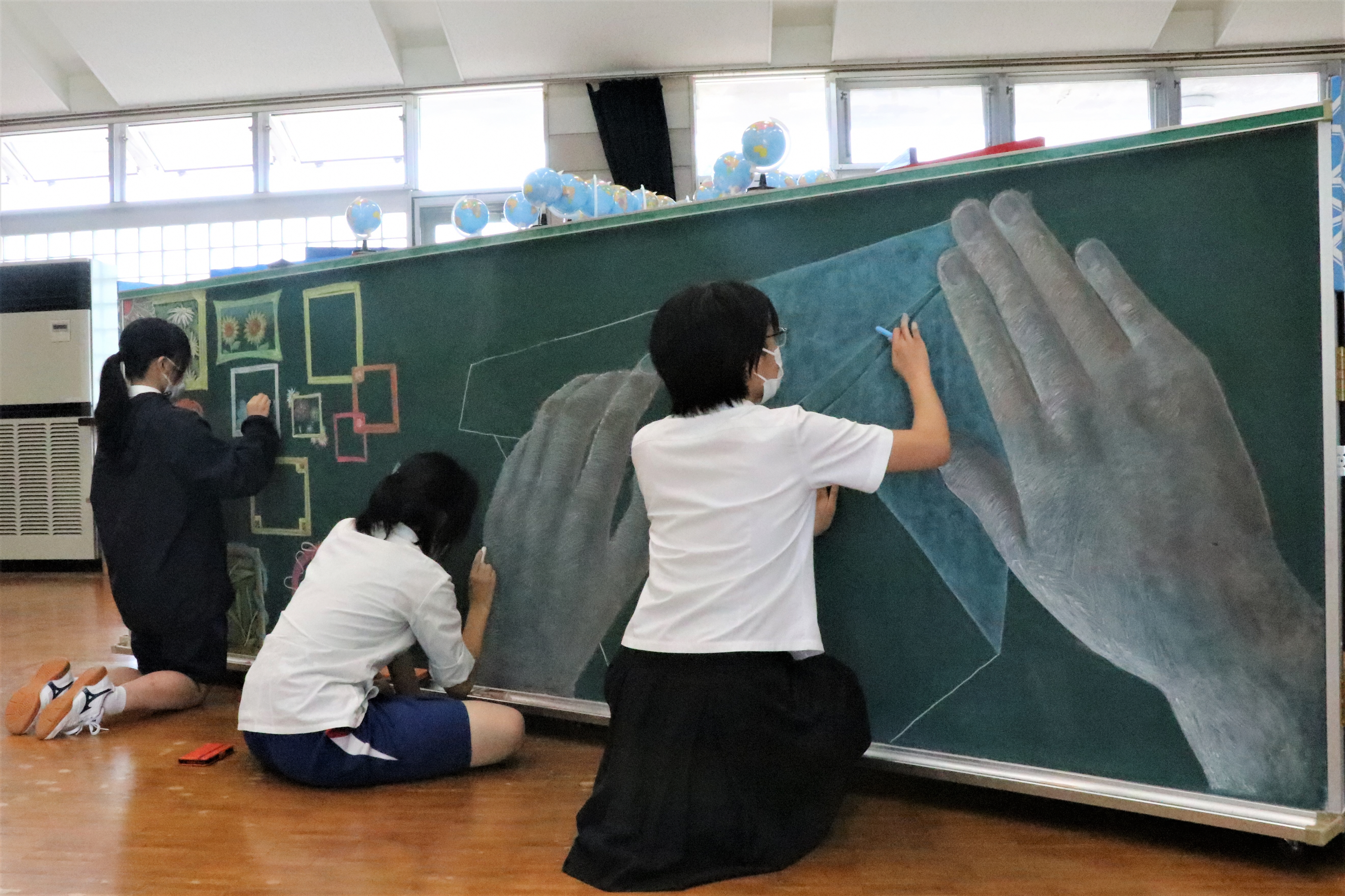 美術部の生徒3人が黒板に描いている様子