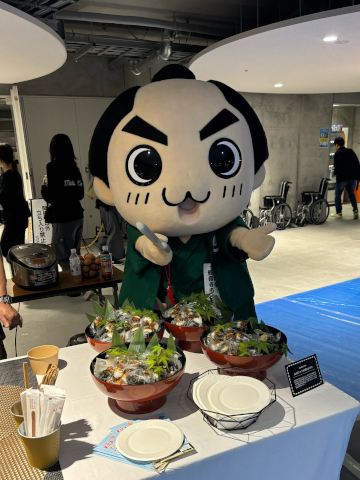 舞台裏で道の駅とよはまのえびじゃこ味噌おにぎりをPRする銭形くん