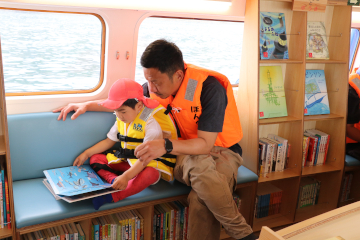 図書館船内で一緒に本を読むお父さんと子ども