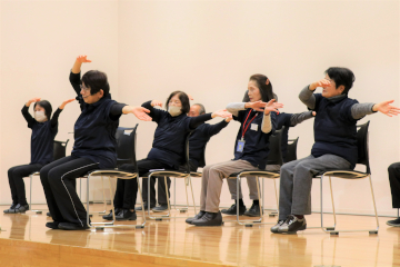 ステージで、いすに座りながらできる介護予防体操を披露する人々